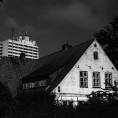 Schwarzweiß-Film-Foto eines sehr alten Hauses im Vordergrund und eines Hochhauses im Hintergrund