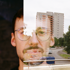 Doppelbelichtung: Portrait eines jungen Mannes zusammen mit Teilen zweier Frames, Blick auf eine Hochhaussiedlung auf einem davon