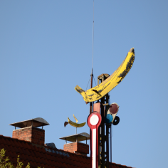 Als Dekoration genutztes Bahnsignal mit einer Banane, dahinter ein H&auml;userdach mit einer Wetterbanane