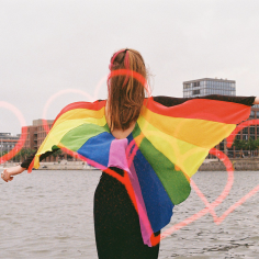 Farbfilmfoto einer blonden Frau mit Regenbogencape, von hinten fotografiert, auf die Kieler H&ouml;rn hinausblickend